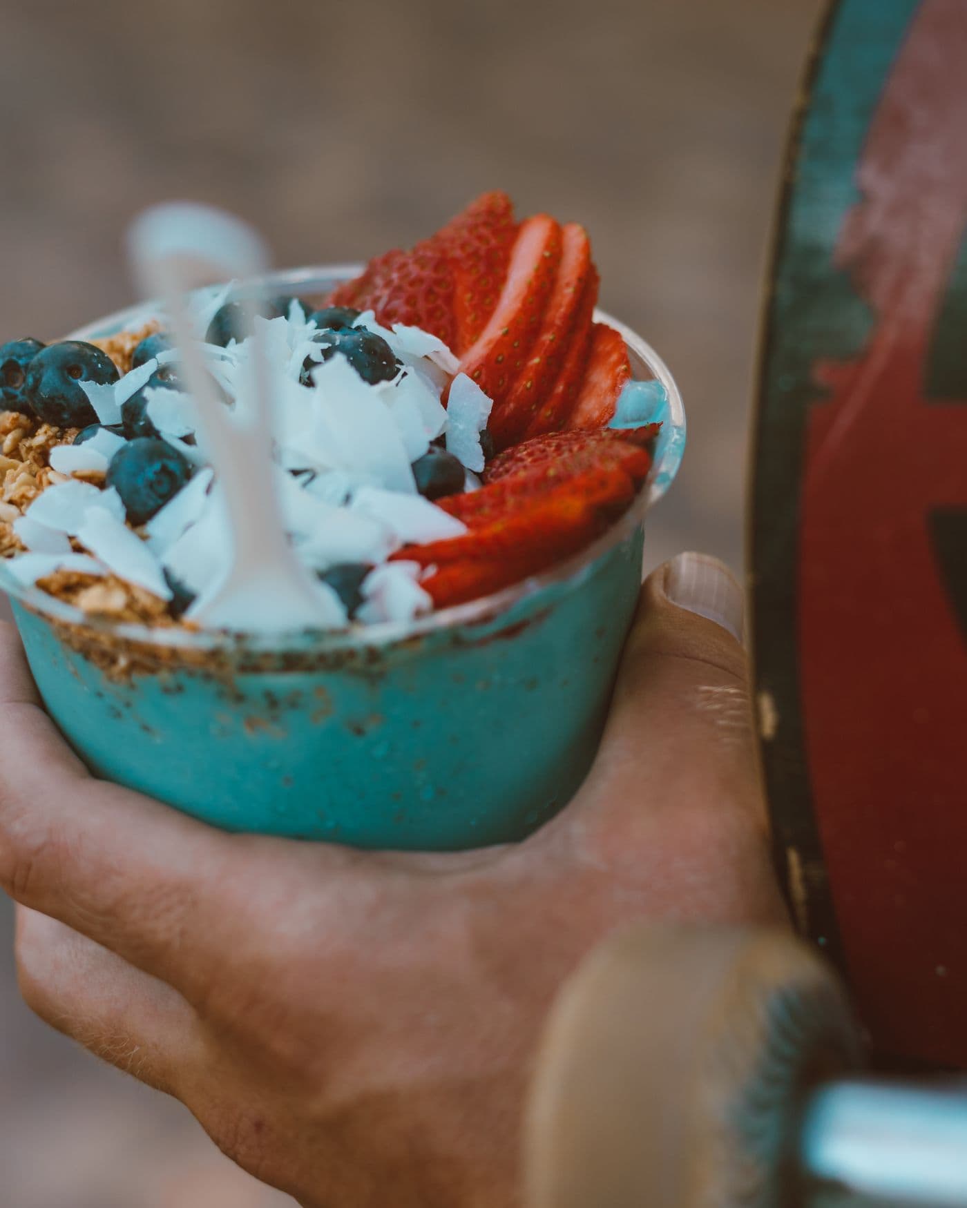 Hands holding an açaí bowl with strawberry and coconut next to a skateboard. Photo by Jess Loiterton (Pexels)